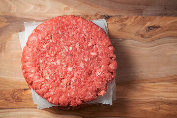 Stack of three fresh uncooked beef burgers separated with cooking paper on a cutting wooden board and table. Food industry. Top down view