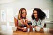 © Prins Productions - Mixed race female friends texting on cellphones chatting together in kitchen bonding