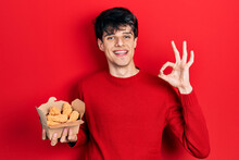 Handsome Hipster Young Man Eating Chicken Wings Doing Ok Sign With Fingers, Smiling Friendly Gesturing Excellent Symbol