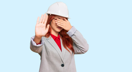 Sticker - Young redhead woman wearing architect hardhat covering eyes with hands and doing stop gesture with sad and fear expression. embarrassed and negative concept.