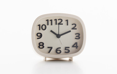 Small white alarm clock, black numbers, set the time for 10.10 o'clock, placed on a white table.