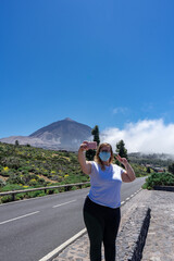 Young tourist woman with mask taking a selfie. In the background you can see Mount Teide, with its 3,178 meters high. This volcano is located in Tenerife, Canary Islands