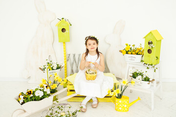 Little girl sitting with basket with fresh flowers on yellow bench look in camera