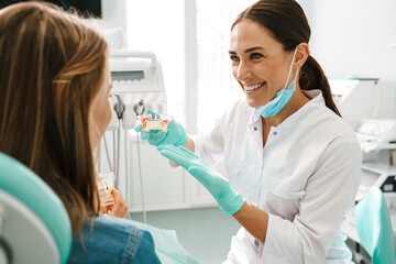 Wall Mural - European mid happy dentist woman showing teeth imitation to her patient