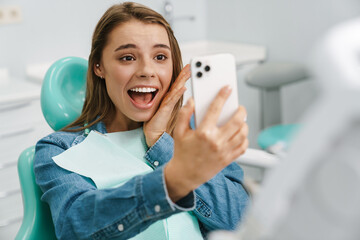 European excited woman taking selfie photo on cellphone at dental clinic