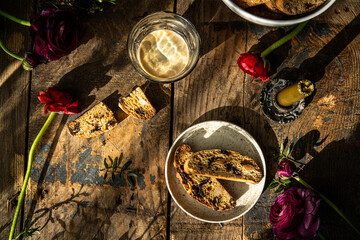 Homemade almond and chocolate biscotti with glass of coffee and  ranunculus flowers on wooden table on dark background.