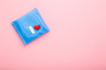 Wall Mural - Bright red heart on blue pack of sanitary towel on light pink table background. Pastel color. Closeup. Protection in day and night time. Empty place for text. Top down view. Copy space.