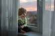 © Tomsickova - Toddler child, sitting on the window on sunset, looking out