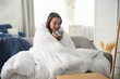 © New Africa - Beautiful young woman wrapped with soft blanket holding cup of hot drink on sofa at home