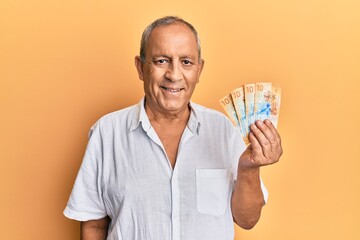 Poster - Handsome mature man holding swiss franc banknotes looking positive and happy standing and smiling with a confident smile showing teeth