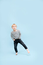Amusing Blond Boy Standing On One Foot, Shifting His Weight. Over Blue