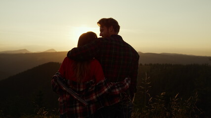 Hikers enjoying sunset in mountains. Romantic couple hugging together outdoor