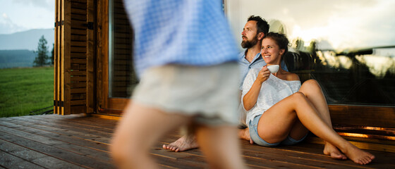 Wall Mural - family with small daughter sitting on patio of wooden cabin, holiday in nature concept.