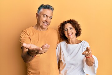 Wall Mural - Beautiful middle age couple together wearing casual clothes smiling cheerful offering palm hand giving assistance and acceptance.