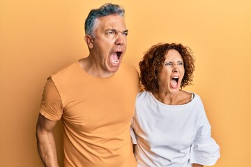 Sticker - Beautiful middle age couple together wearing casual clothes angry and mad screaming frustrated and furious, shouting with anger. rage and aggressive concept.