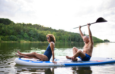 Sticker - Senior couple paddleboarding on lake in summer.
