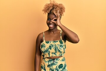 Poster - Young african woman with afro hair wearing summer dress doing ok gesture with hand smiling, eye looking through fingers with happy face.