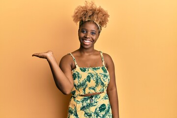 Poster - Young african woman with afro hair wearing summer dress smiling cheerful presenting and pointing with palm of hand looking at the camera.