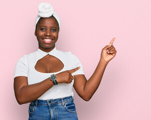 Canvas Print - Young african woman with turban wearing hair turban over isolated background smiling and looking at the camera pointing with two hands and fingers to the side.