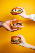 Hands Holding Burger Against Yellow Background. Fast Food, Junk Food Concept.