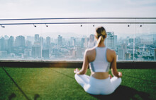 Young Woman Meditating On Roof Of Skyscraper