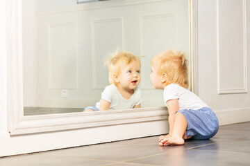 Little toddler boy play with big mirror on wall