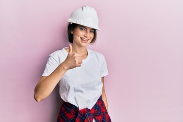 Poster - Young caucasian woman wearing hardhat doing happy thumbs up gesture with hand. approving expression looking at the camera showing success.