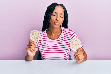 Beautiful hispanic woman eating healthy rice crackers looking at the camera blowing a kiss being lovely and sexy. love expression.