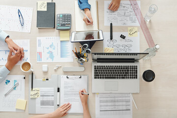 Wall Mural - Marketing team working on project at table with charts, documents and gadgets, view from the top