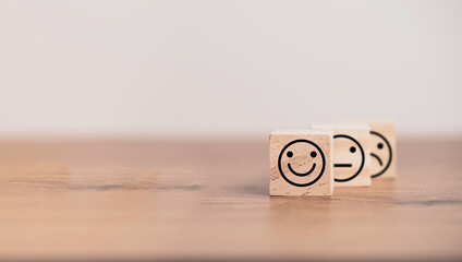 Wall Mural - Smiley face in front of normal and sadness face which print screen on wooden cube block, emotion selection for customer satisfaction and evaluation concept.