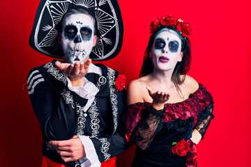 Poster - Young couple wearing mexican day of the dead costume over red looking at the camera blowing a kiss with hand on air being lovely and sexy. love expression.