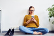 © baranq - Young businesswoman sitting using mobile phone sitting on floor in office