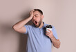 Sleepy young man with cup of coffee yawning on beige background