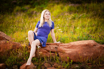 Beautiful young blonde in blue dress sitting on red rocks, Selective focus