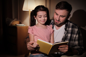 Wall Mural - Little girl with father reading fairy tale at home in evening