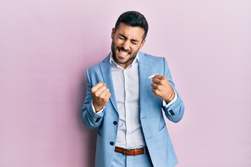 Young hispanic businessman wearing business jacket very happy and excited doing winner gesture with arms raised, smiling and screaming for success. celebration concept.