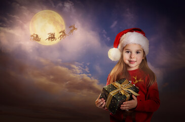 Wall Mural - Cute child with Christmas gift and Santa Claus flying in his sleigh on background