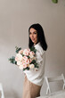 © Natalia - brunette in a white shirt beige pants with a bouquet of flowers on a wall background