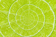 Top View Of Textured Ripe Slice Of Organic Lime Citrus Fruit With Spiral Endless Fine-skinned. Cool Green Lemon Citrus Fruit Background.