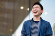 © whyframeshot - happiness cheerful asian male casual cloth standing outdoor laughing wide mouth fun and positive emotional with modern building window glass wall background
