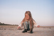 Little girl with blond hair plays with sand on the beach