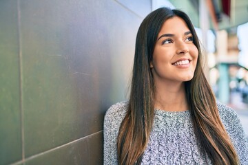 Poster - Young beautiful hispanic girl smiling happy leaning on the wall at the city.