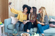 © nenetus - Smiling entrepreneur multiethnic women making a selfie with smart phone sitting on couch at coworking place.