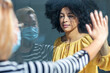 © nenetus - Two friends touching her hands separated by a glass window for social distancing during the corona virus pandemic.