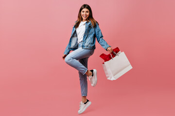 Pleased young woman holding store bag. Full length view of charming european girl in denim attire.