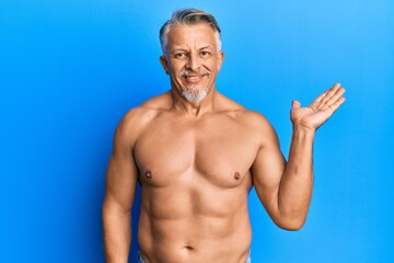 Sticker - Middle age grey-haired man standing shirtless smiling cheerful presenting and pointing with palm of hand looking at the camera.