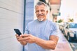 Middle age hispanic grey-haired man smiling happy using smartphone at the city.