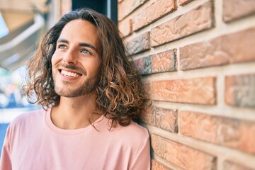 Poster - Young hispanic man smiling happy looking to the side leaning on the wall