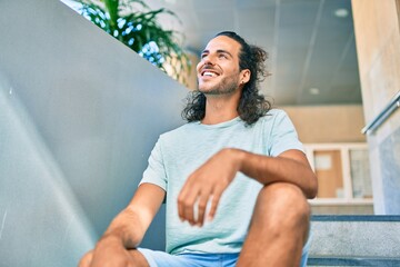 Sticker - Young hispanic man smiling happy looking to the side and sitting on the stairs.