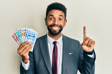 Sticker - Handsome hispanic man with beard wearing business suit holding yuan banknotes smiling with an idea or question pointing finger with happy face, number one